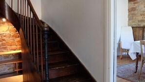 A wooden staircase with a stone wall on one side and a white door leading to a room with a chair and a table. - The Hauts de Kerity, 1920's house by the sea (Paimpol)