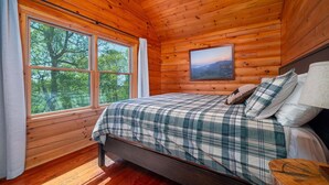 Un dormitorio de cabaña de madera con una cama, un ventanal y un cuadro en la pared.