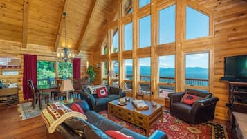 Relax in a spacious living area with expansive views of the surrounding landscape, featuring a leather sofa, smaller couch, and mounted TV.