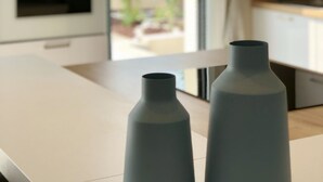 Eine moderne Küche mit weißen Schränken, einem eingebauten Ofen und Blick auf einen Garten durch das Fenster.