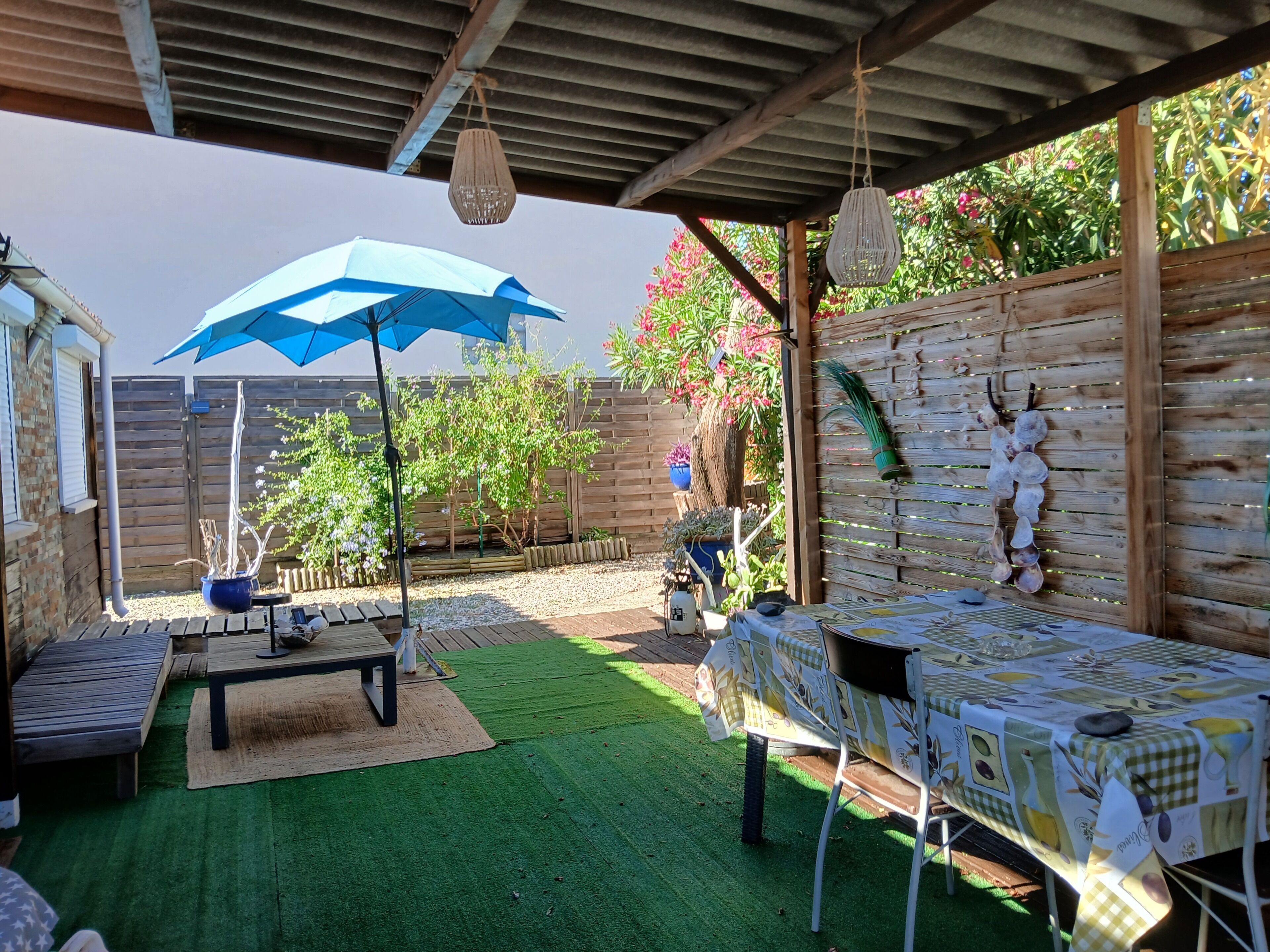Une terrasse couverte avec une table et des chaises, un luminaire suspendu et une clôture en bois.