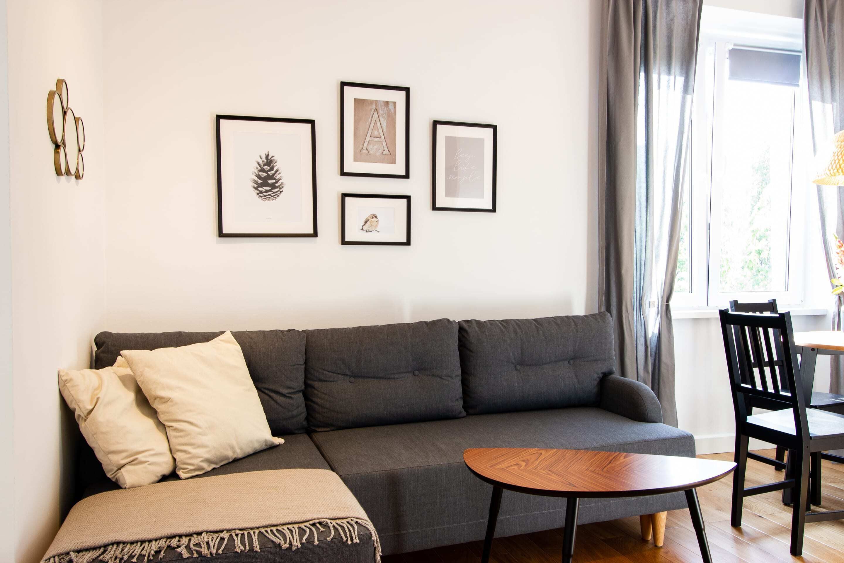 Un salon moderne avec un canapé gris, une table basse en bois et une collection d’œuvres d’art encadrées accrochées au mur.