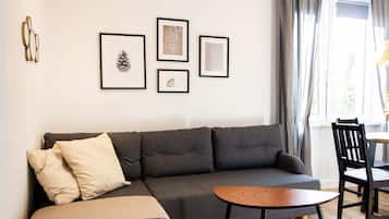 Un salon moderne avec un canapé gris, une table basse en bois et une collection d’œuvres d’art encadrées accrochées au mur.