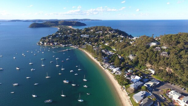 An aerial view of a coastal area with a marina, houses, and a forested hill.