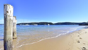 A sandy beach with a wooden post in the foreground and several boats anchored in the water.