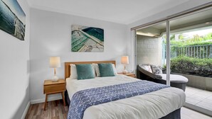 A bedroom with a bed, two bedside tables with lamps, a large window, and a balcony with plants.