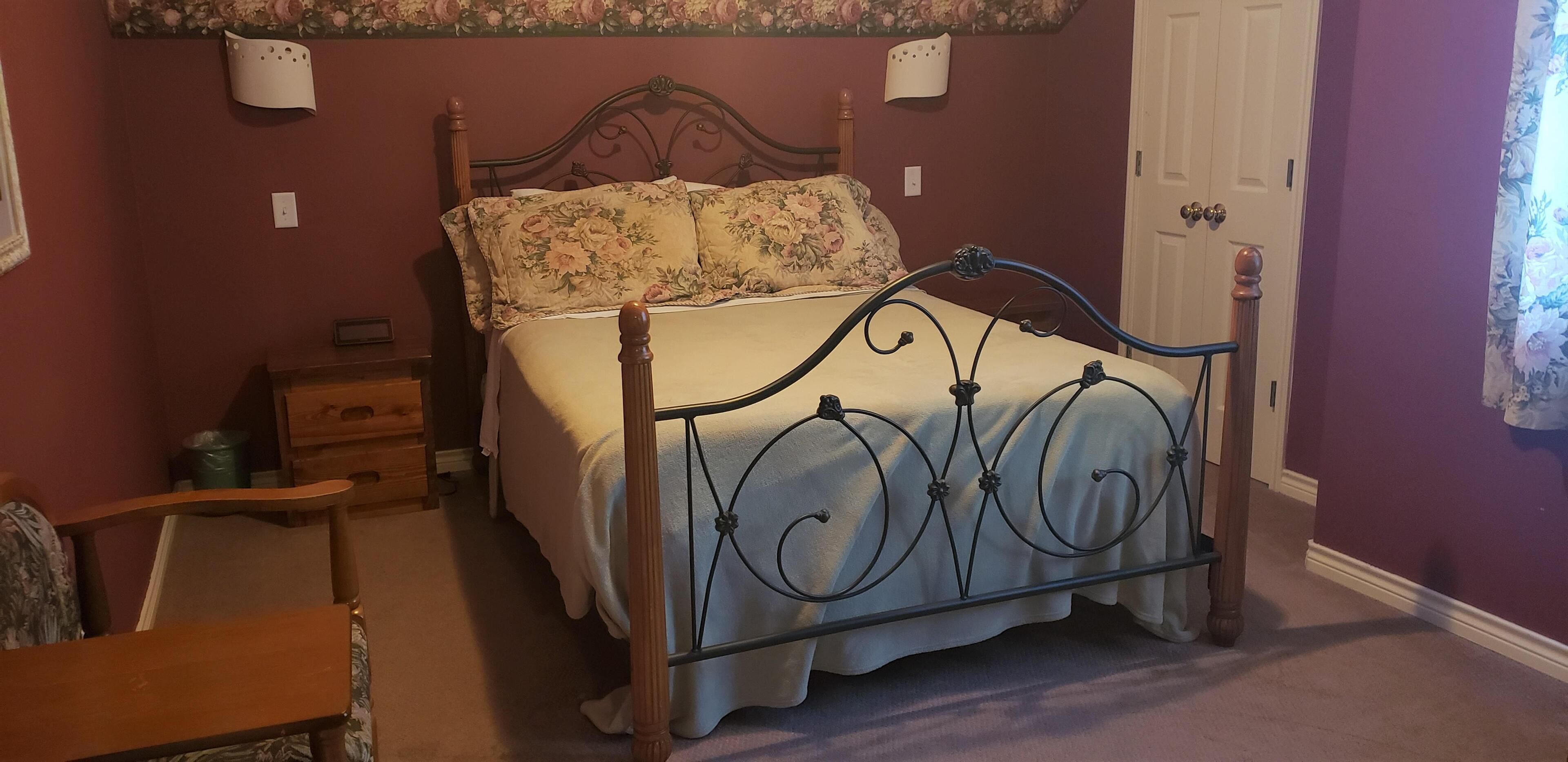 Ein Schlafzimmer mit einem Himmelbett, einem Holfnachtkästchen, einem Stuhl und einer Tür.