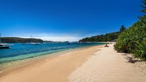 Une plage à l’eau turquoise et limpide, avec des bateaux et une rive sablonneuse.