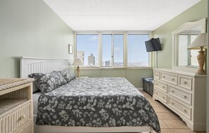 Quarto com cama, penteadeira, televisão e janela com persianas.
