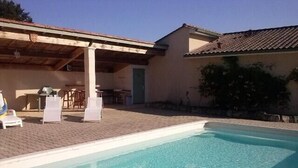 Une piscine avec des chaises longues et un espace patio couvert.