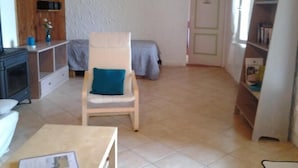 Une petite pièce agréable, avec un meuble en bois, une chaise blanche dotée d’un coussin bleu, un lit recouvert d’une couverture grise et une bibliothèque.