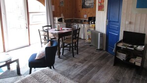 Een gezellige kamer met houten inrichting, een eettafel met stoelen, een kleine kitchenette en een blauwe deur.