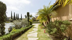 A garden pathway leading to a building with a stone facade, surrounded by various plants and trees.