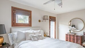 A bedroom with a bed, a nightstand, a dresser, a ceiling fan, a window with blinds, and a wall-mounted lamp.