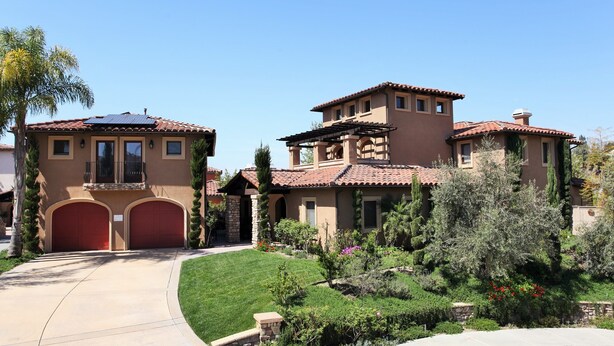 A two-story house with a red garage, a balcony, and a solar panel on the roof.
