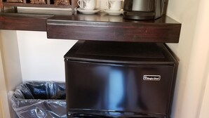 A compact kitchen area with a black refrigerator, a coffee maker, and a trash bin.