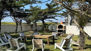 An outdoor patio with wooden furniture, including chairs and a table, surrounded by trees and a barbecue area. - Villa Des Dunes, feet in the water! (Brétignolles-sur-Mer)