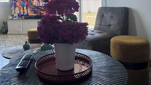 A living room with a large TV displaying a Cuba-themed show, a potted plant, a grey armchair, and a sign that says "SURF THIS WAY". - Villa Des Dunes, feet in the water! (Brétignolles-sur-Mer)