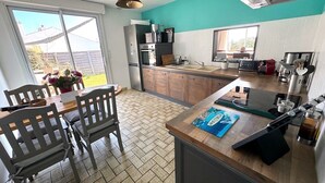 A modern kitchen with a large island, wooden cabinets, and a view of the backyard through a sliding door. - Villa Des Dunes, feet in the water! (Brétignolles-sur-Mer)