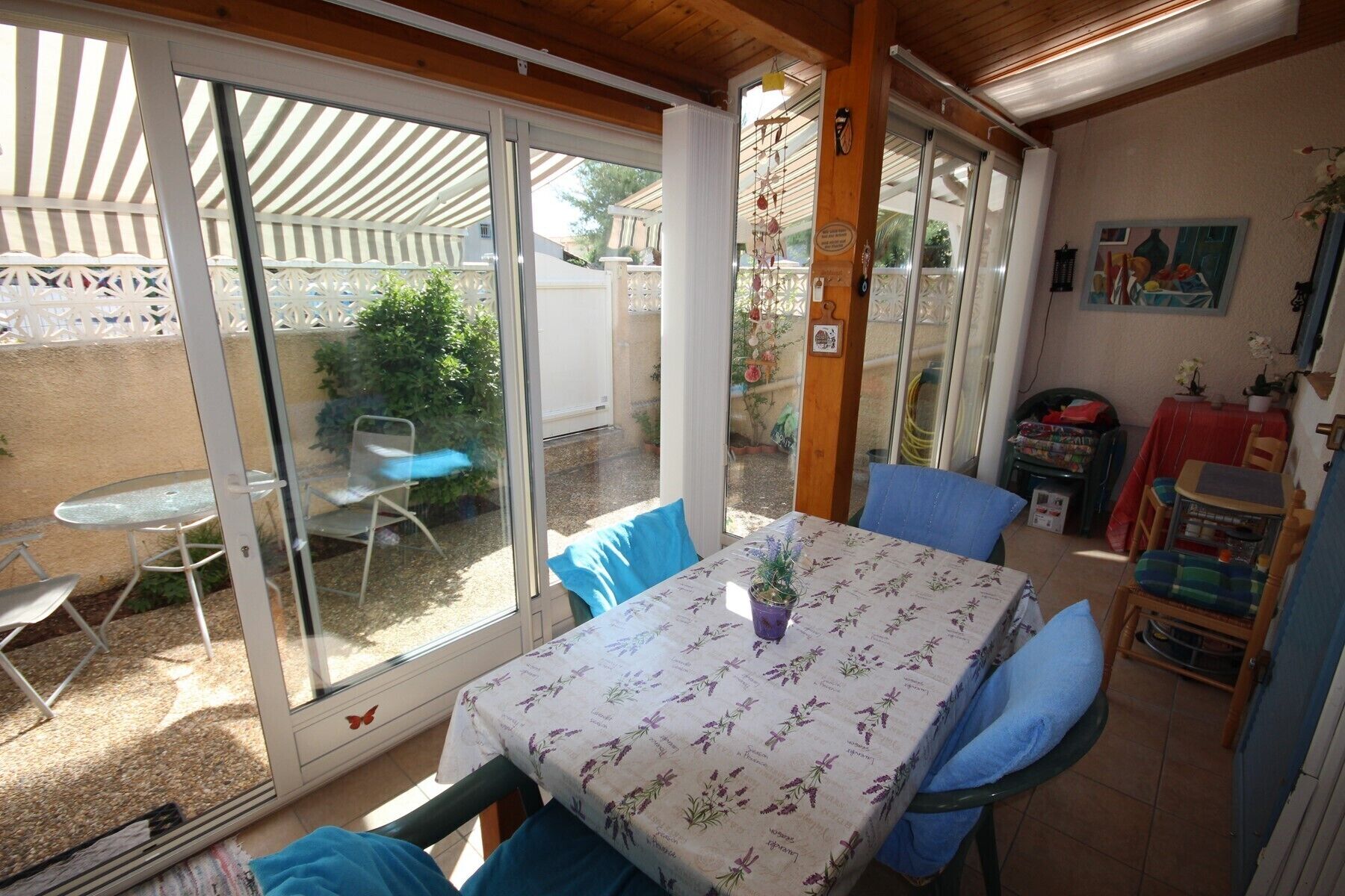 A covered patio with a table and chairs, a sliding glass door leading to a garden, and a small table with a vase.