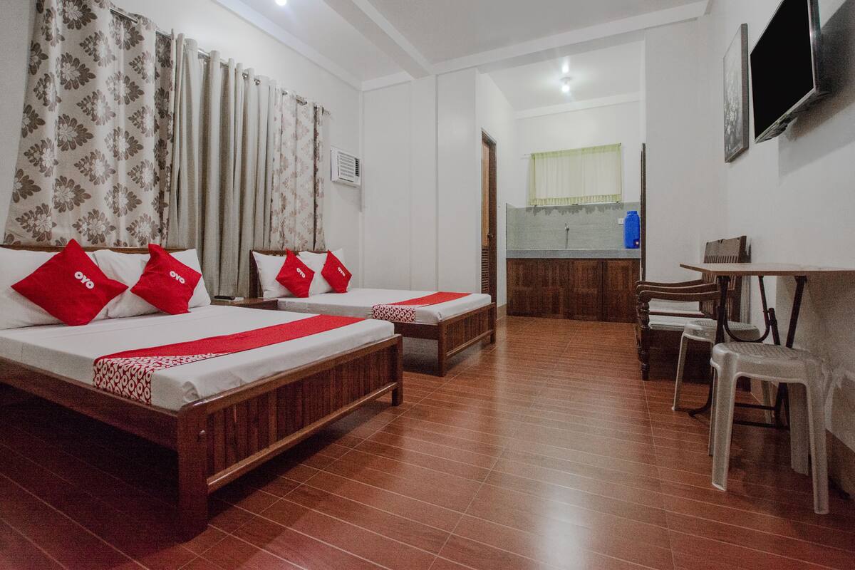 A hotel room with two beds, a small kitchenette, a TV, and a dining area.