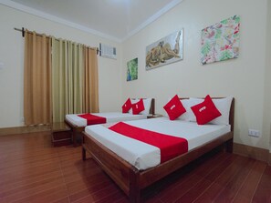 Habitación de hotel con dos camas, suelo de madera, cortina, aire acondicionado y dos obras de arte en la pared.