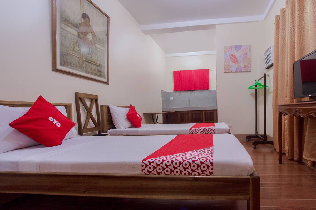 A hotel room with two beds, each with white bedding and red accents, a television, and a painting on the wall.