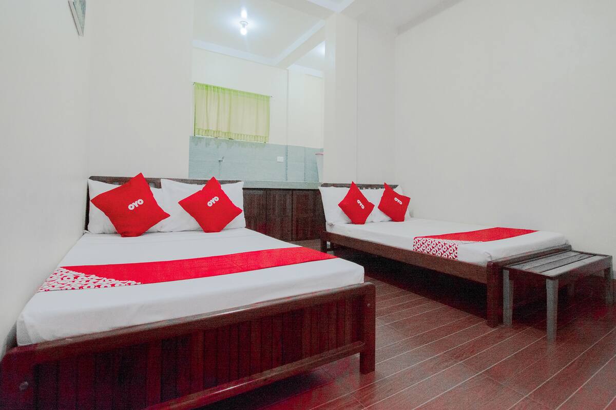 A hotel room with two beds, each with a red 'oyo' pillow, a wooden headboard, and a white bedspread.