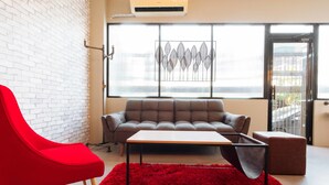A modern living room with a red chair, a grey sofa, and a red rug. - RedDoorz Plus near Osmena Highway 2 - Quarantine Hotel (Manila)