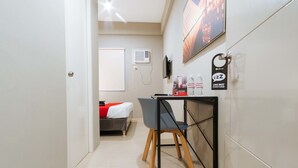 A hotel room with a bed, a desk with a chair, a wall-mounted TV, a window, and a door. - RedDoorz Plus near Osmena Highway 2 - Quarantine Hotel (Manila)