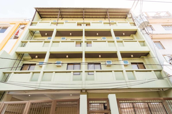 Un immeuble à plusieurs étages doté de balcons, de climatiseurs et d’une entrée sécurisée par un portail.