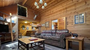 Un interior de cabaña acogedor con suelo de madera, un sofá, una mesa de centro, un televisor y una araña.