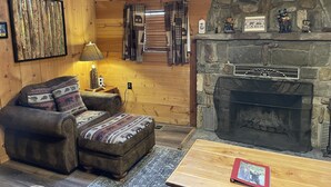 Un interior acogedor de cabaña, con paredes de madera, una chimenea de piedra, un sofá y una pequeña mesa.