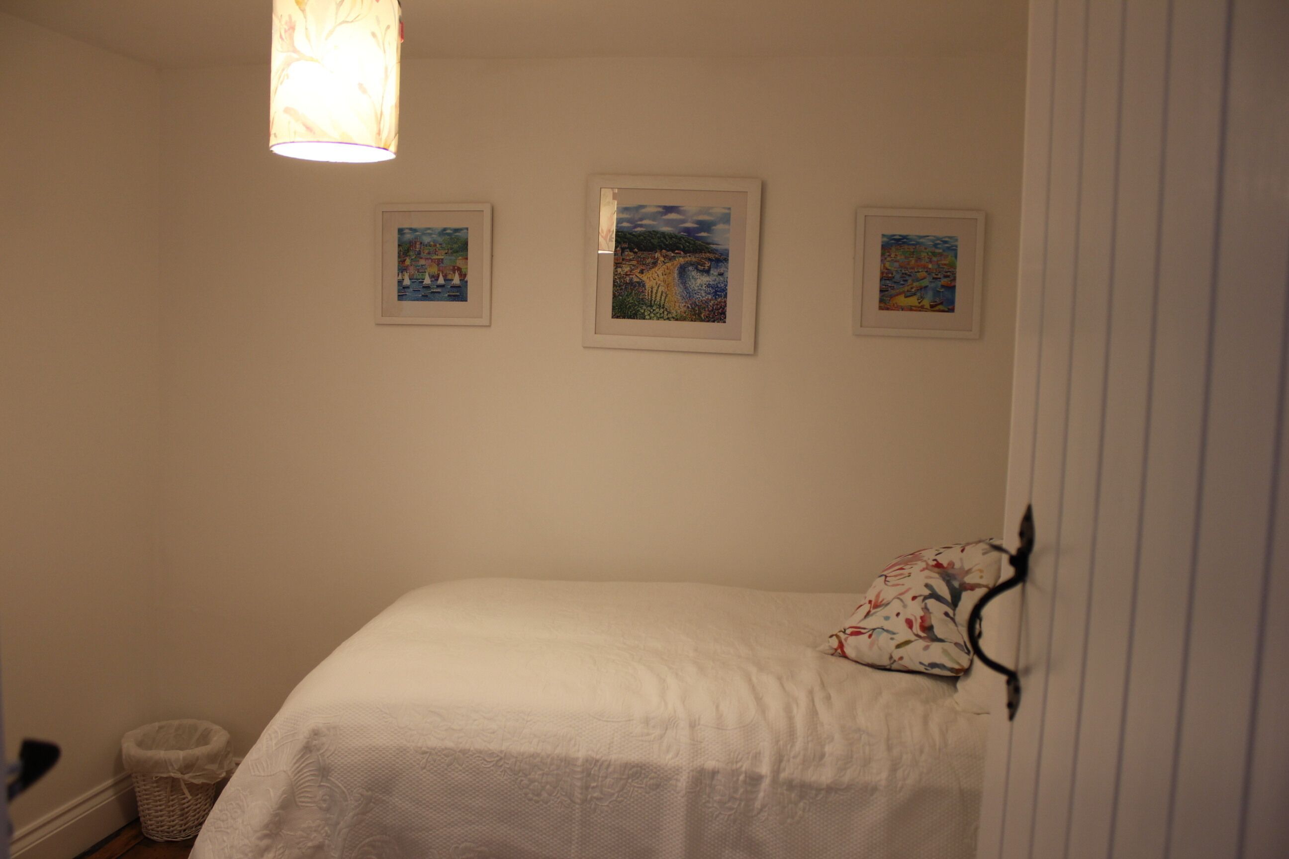 A bedroom with a bed, a hanging light fixture, and three framed pictures on the wall.