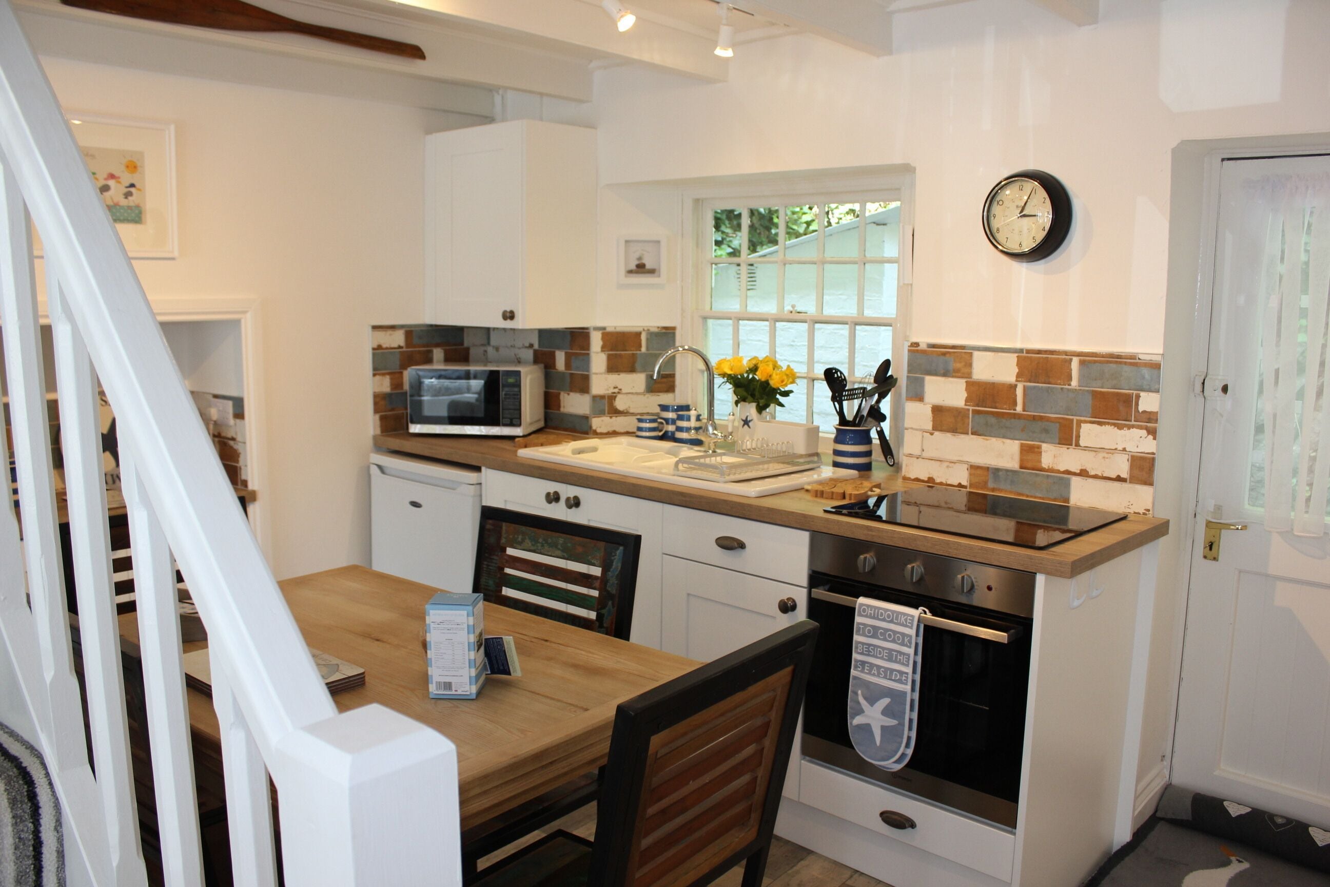 A compact kitchen with a microwave, oven, and a clock on the wall.