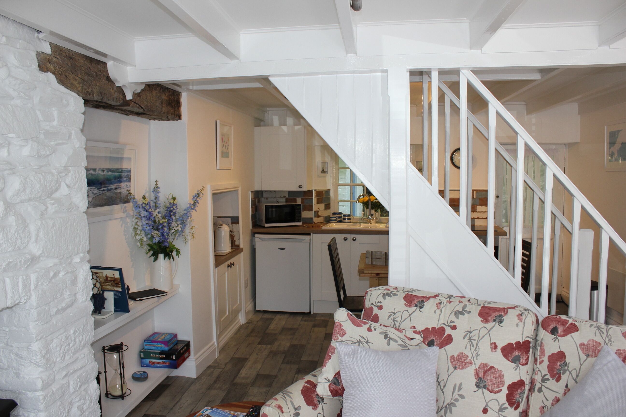 A cozy living room with a floral sofa, a small kitchen area with a microwave, and a staircase leading to another level.