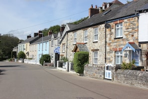 A row of traditional stone buildings with a clear road in front. - Lil' Nauti (St Austell)
