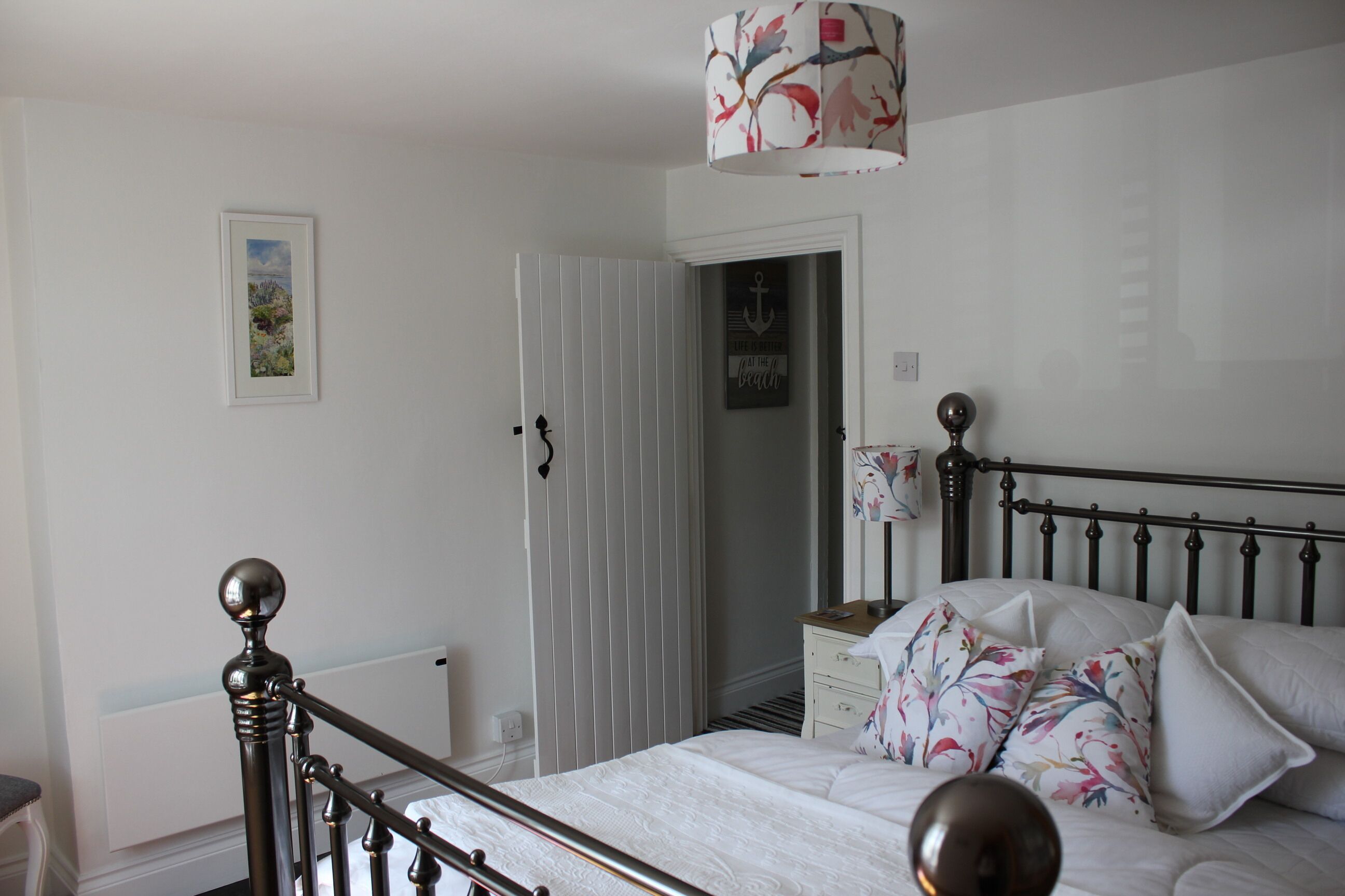 Un dormitorio con cama, mesita de noche, lámpara y puerta que da a otra habitación.