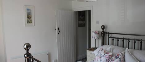 Un dormitorio con cama, mesita de noche, lámpara y puerta que da a otra habitación.