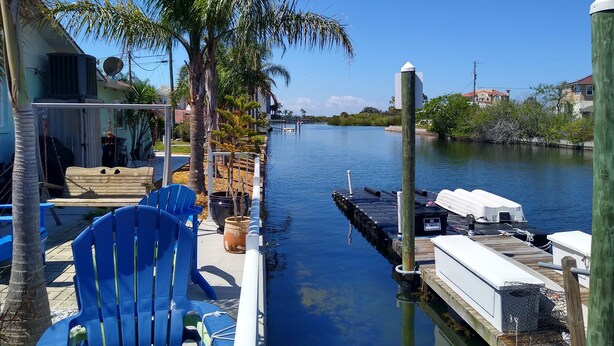 A dock with a boat, a blue chair, and a palm tree. - Waterfront-canal/w/Gulf view-pets welcome-private dock for a fee. (Hudson)