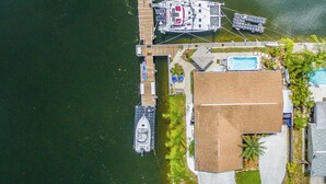 An aerial view of a docked boat, a swimming pool, and a house with a large deck area. - Waterfront-canal/w/Gulf view-pets welcome-private dock for a fee. (Hudson)