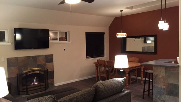 A living room with a fireplace, a television, a ceiling fan, and a dining area with a table and chairs. - Location! Historical District Downtown - Walk everywhere, new 4 Bedroom, 3 Bath (Bend)