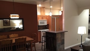 A modern kitchen with wooden cabinets, a microwave, and a built-in stove. There is a dining area with a wooden table and chairs, and a bar area with stools. - Location! Historical District Downtown - Walk everywhere, new 4 Bedroom, 3 Bath (Bend)