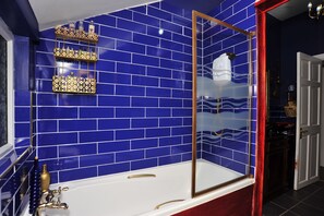 A bathroom with blue tiled walls, a white bathtub, and gold fixtures. - The Beauty Rooms (Liverpool)