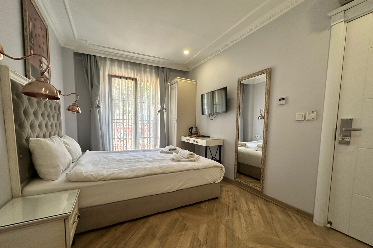 A hotel room with a large bed, a bedside table, a desk, a mirror, a TV, and a door.