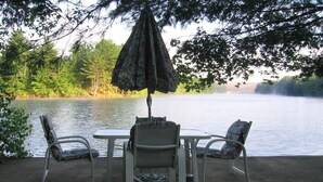 A patio with a table and four chairs, overlooking a calm lake. - Beach cottage on the water - private and pet friendly! (Franklin)