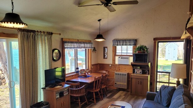 A cozy living room with a wooden dining table, a sofa, and a television. There is a ceiling fan and a window with curtains. - Beach cottage on the water - private and pet friendly! (Franklin)