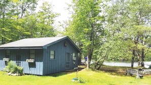 A rustic cabin with a sloped roof, surrounded by lush greenery and a lake. - Beach cottage on the water - private and pet friendly! (Franklin)