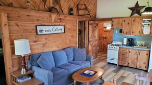 A cozy cabin interior with a blue sofa, wooden table, and kitchen area. - Beach cottage on the water - private and pet friendly! (Franklin)