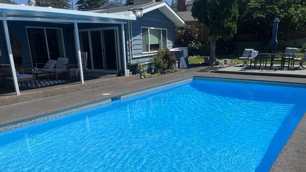 A clear blue swimming pool with a covered patio area and outdoor seating. - Swimming pool, Family friendly home! (Penticton)